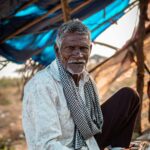Portrait of a senior man sitting outdoors in a rural Indian setting.